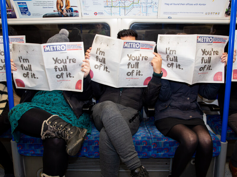 People sat on a train reading a newspaper with a BHF campaign on the cover