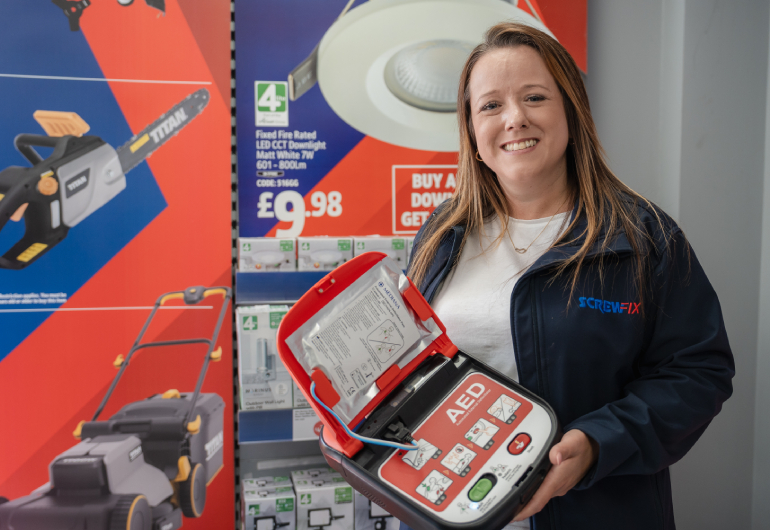 Clare, a Screwfix employee, holding a defibrillator in store.