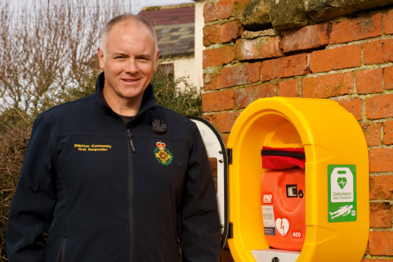 Julian is standing in front of a wall with a defibrillator