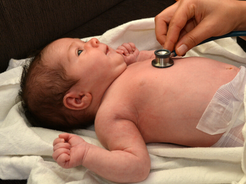 Newborn baby lying on their back and a doctor uses a stethoscope to hear the baby's heart