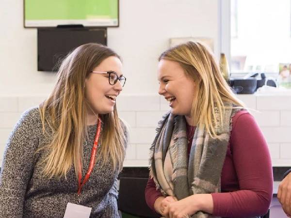 Two teenage girls with BHF lanyards around their necks sitting next to each other and laughing