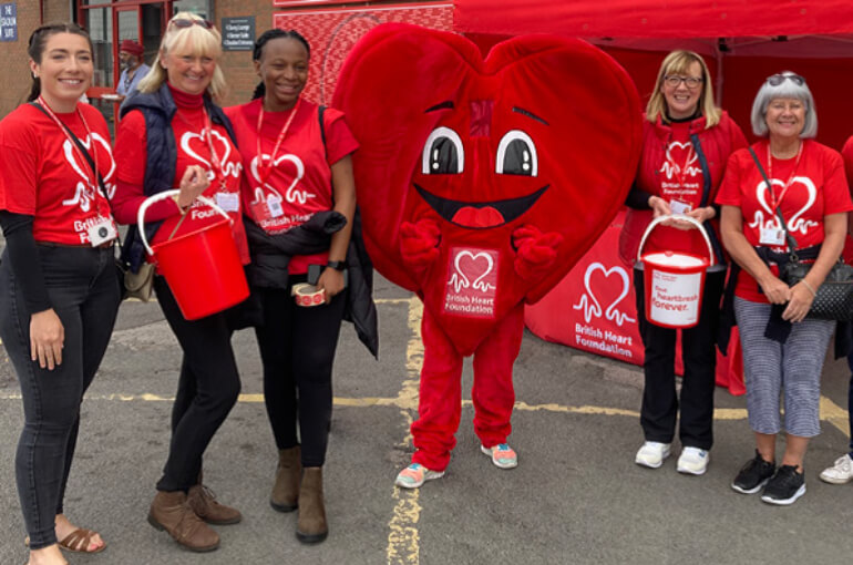 Fundraising volunteers wearing BHF t-shirts and holding collection buckets pose with BHF Heart mascot