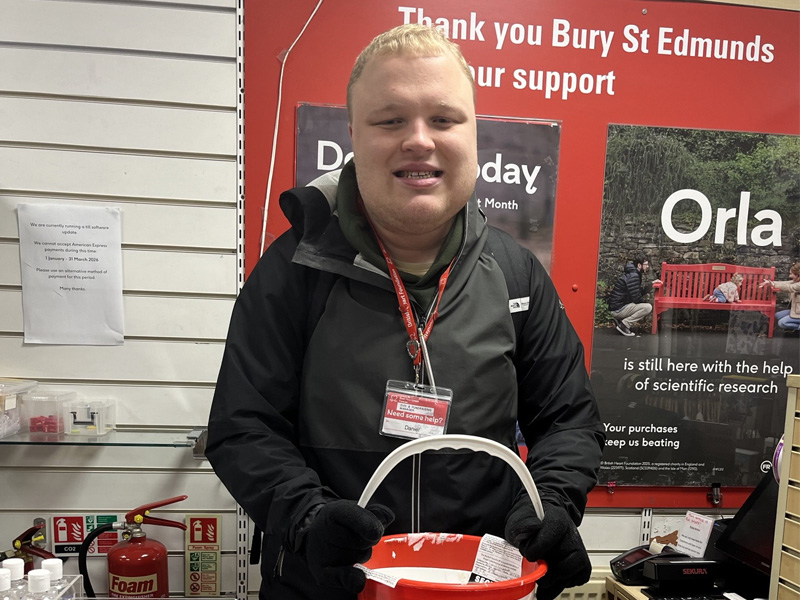 Daniel behind the till at the Bury St Edmunds shop with a collection bucket