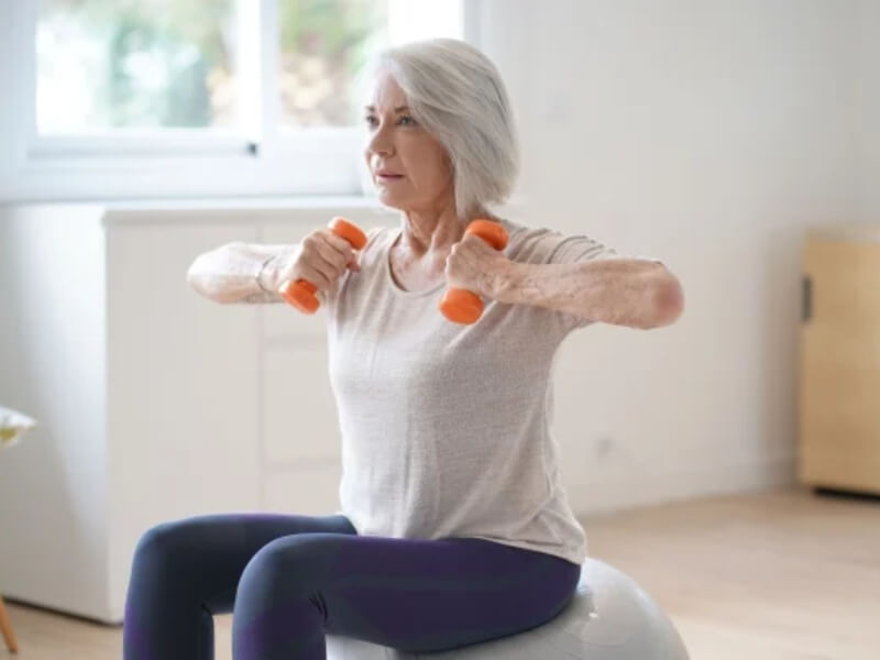 A woman sat on an exercise ball lifting weights