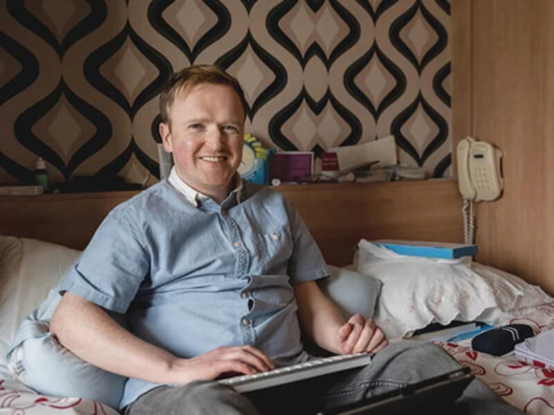 A man sat in bed on his laptop smiling