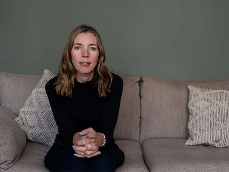 A woman with her hands clasped together leaning in on a sofa