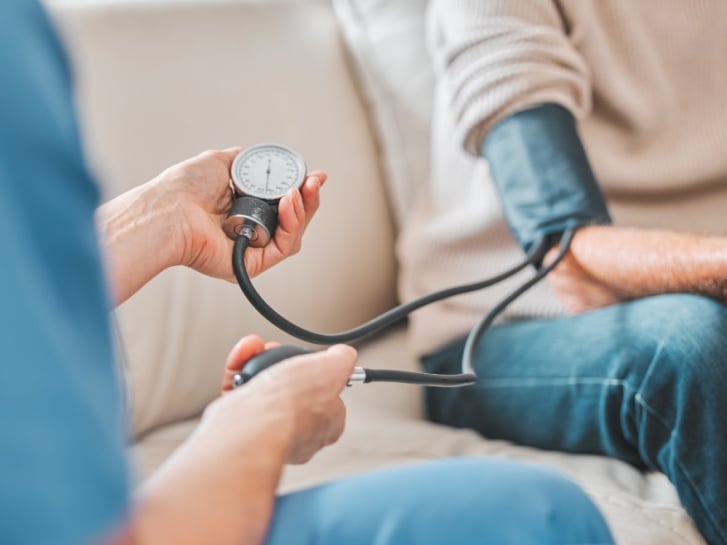 A nurse taking a patients blood pressure while sat on a sofa.