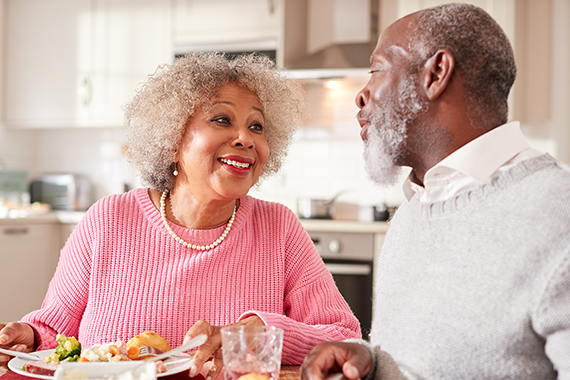 Two adults smile at each other whilst eating a meal together