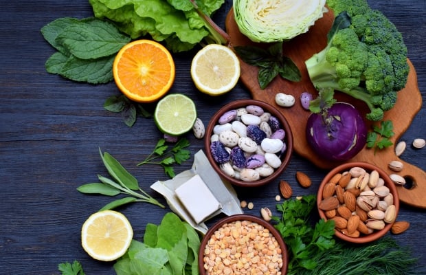 Image of green leafy vegetables and bowls of wholegrains on a dark wooden table