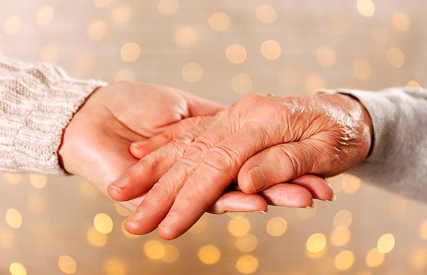 An elderly woman holds on to another woman's hand, with twinkly lights behind them