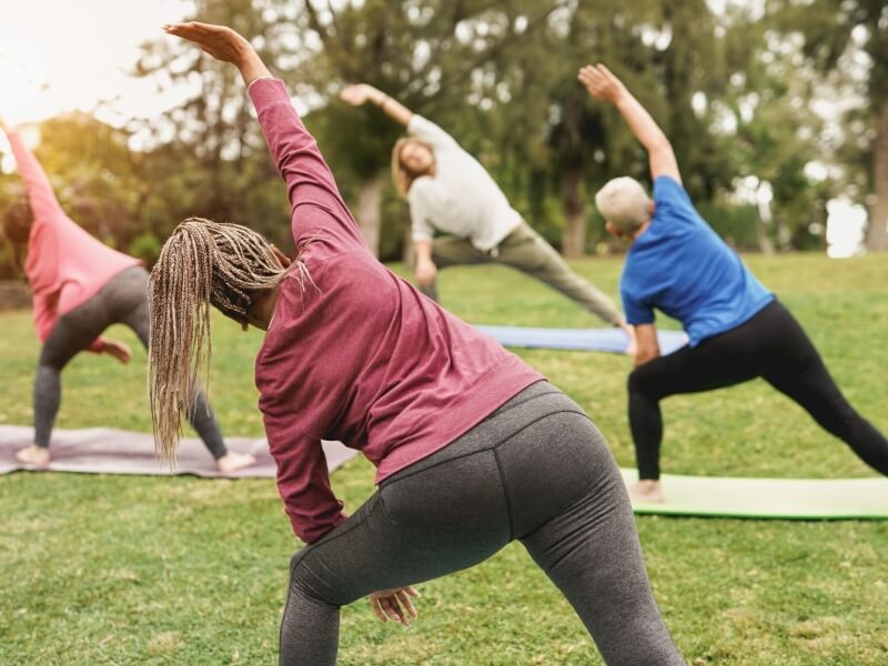 A group of 4 people stretching in a sunny park.