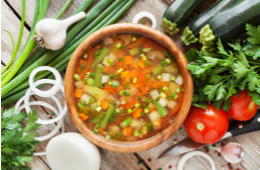 A top down image of vegetable soup, surrounded by fresh vegetables