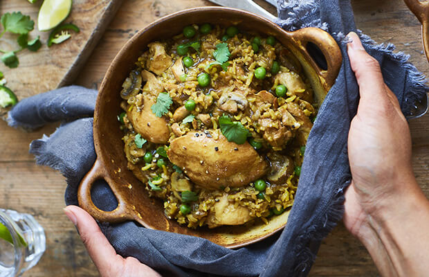Baked chicken and vegetable biryani in a dish on a wooden table