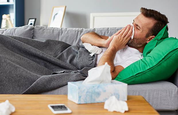 Man sick on the sofa, surrounded by tissues