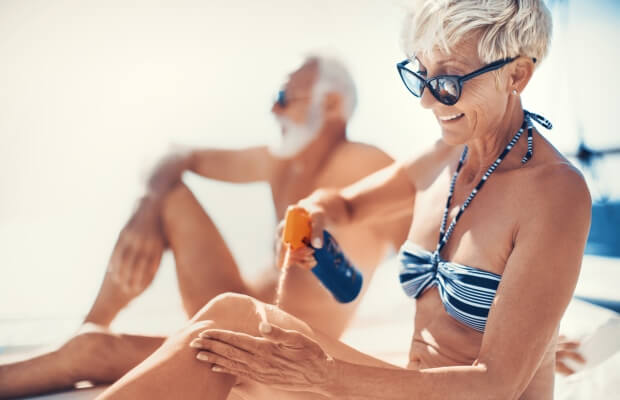 Couple sunbathing on the beach. The woman is applying sun lotion