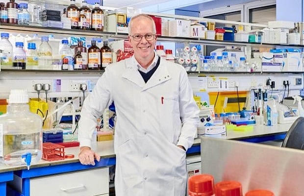 Professor James Leiper standing in a white lab coat, in a lab