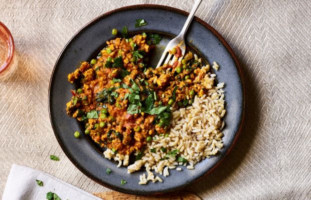 Turkey curry with peas and baby spinach, served with rice and coriander leaves. Presented on a table with a pale patterned tablecloth.