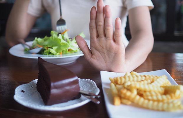 Woman with salad declining cake and chips