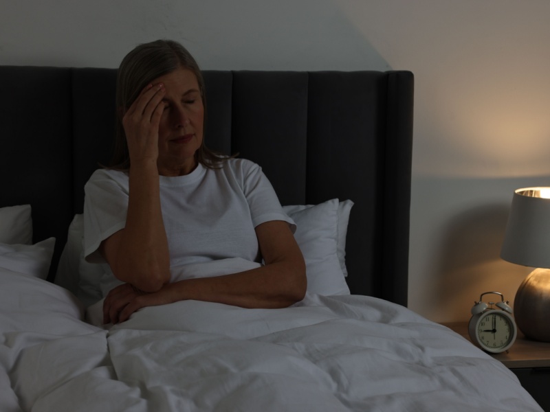 A woman sat in bed at night looking tired.