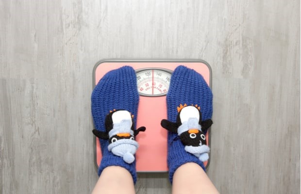 Top view of someone's feet in purple socks with a penguin motif standing on some pink weighing scales.
