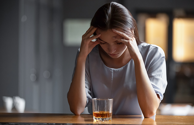 Woman with her hands on her head with a whiskey in front of her