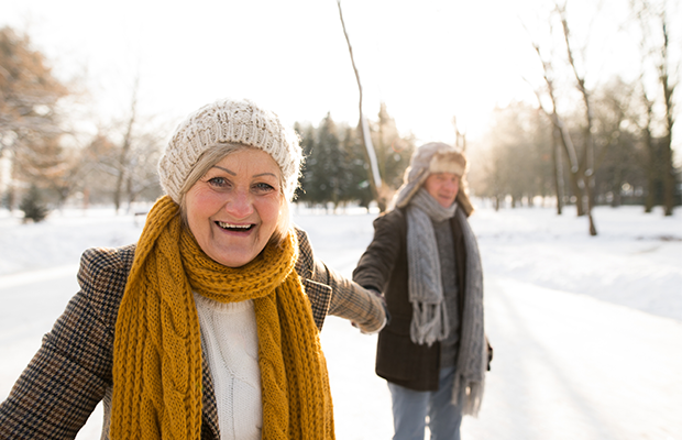 Two people wearing wolly hats and scarves hold hands in the snow