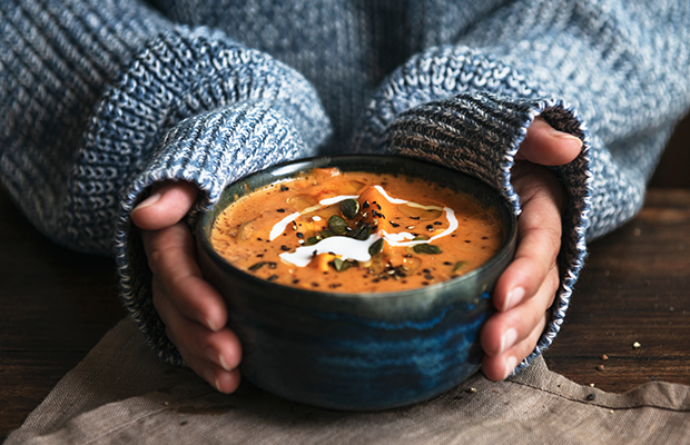 Hands half covered by a knitted jumper hold a bowl of soup