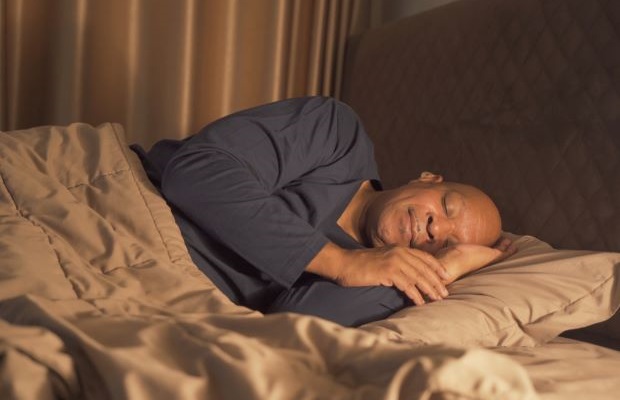 A man wearing navy blue pyjamas is sleeping in bed.