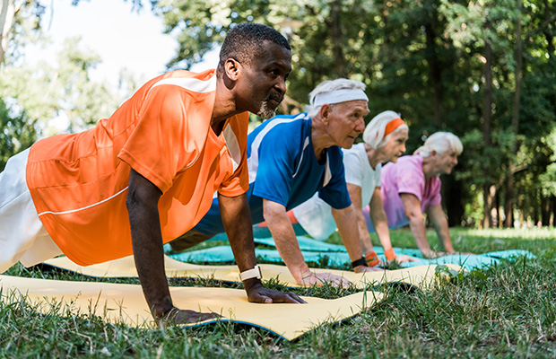 A group of people, lined up in a row, holding the plank position on the grass outdoors