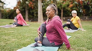 A group of women do stretches on yoga mats outside.