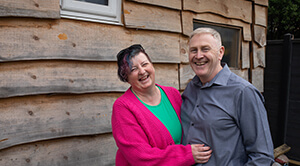 Maggie Sewell laughs with her hands around her husband Rob in front of a wooden building