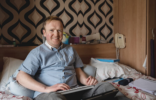 Patrick McCann sits on his bed typing on a keyboard on his lap