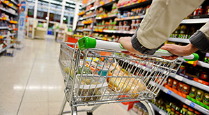 A metal shopping trolley with some items in it being pushed down an aisle by a man
