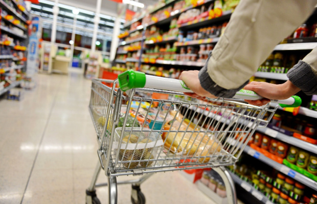 A metal shopping trolley with some items in it being pushed down an aisle by a man