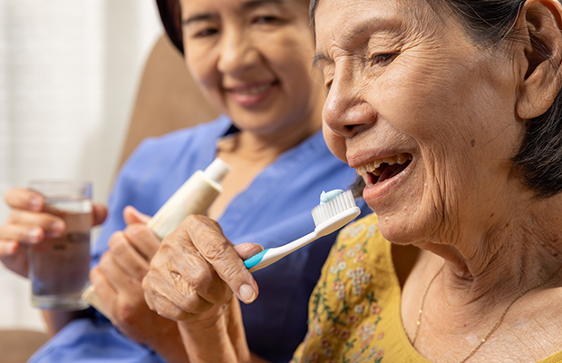 Elderly woman brushing her teeth with support of a nurse
