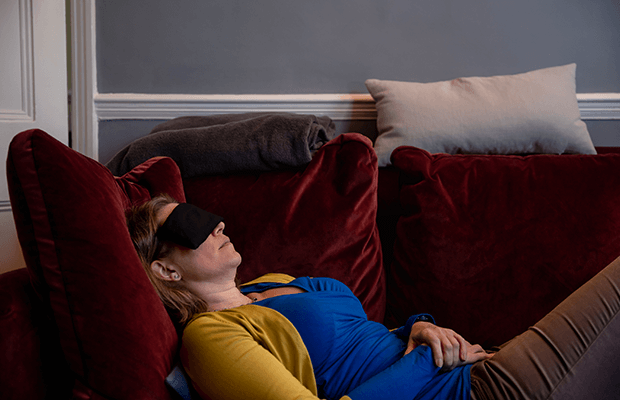 Kerstin Sailer lying down on a red velvet sofa wearing a sleep mask over their eyes