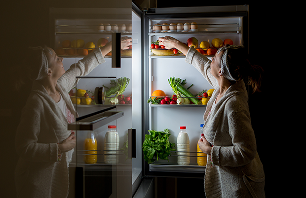 Photograph of woman grabbing a midnight snack from the fridge late at night