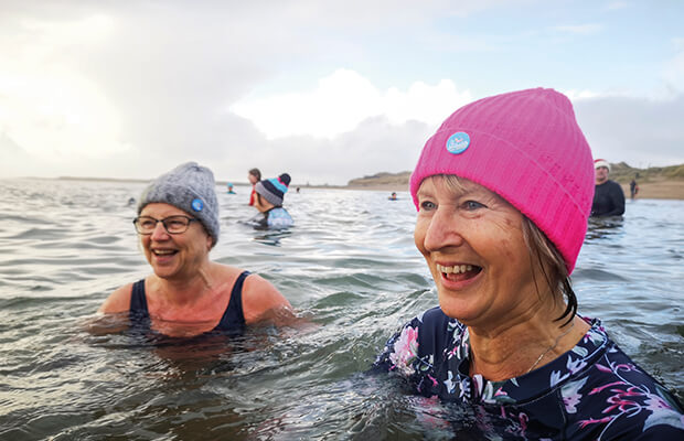 A group of swimmers wearing woolly hats smile in the sea.