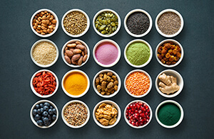 Small bowls containing acai powder, turmeric, matcha, pomegranate, blueberries and other superfoods