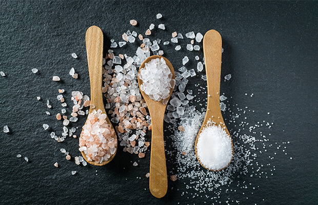 Three wooden spoons with different types of salt spilling over each spoon