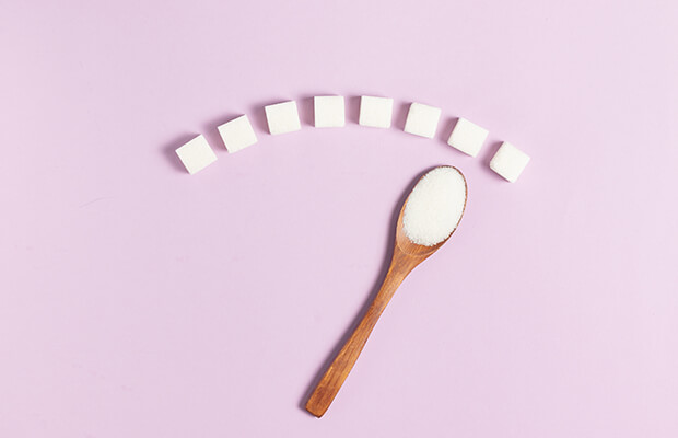 Eight sugar cubes in a curve above a wooden teaspoonful of granulated sugar