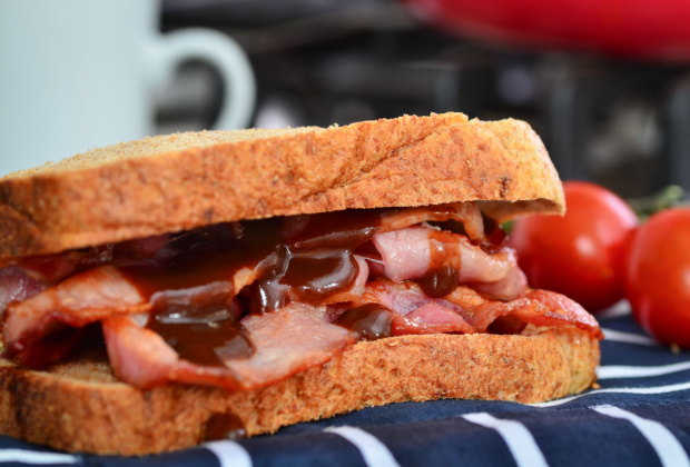 A brown bread bacon sandwich with brown sauce squeezed over it
