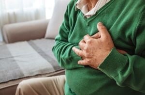 A person sits on a sofa with their hands on their chest.