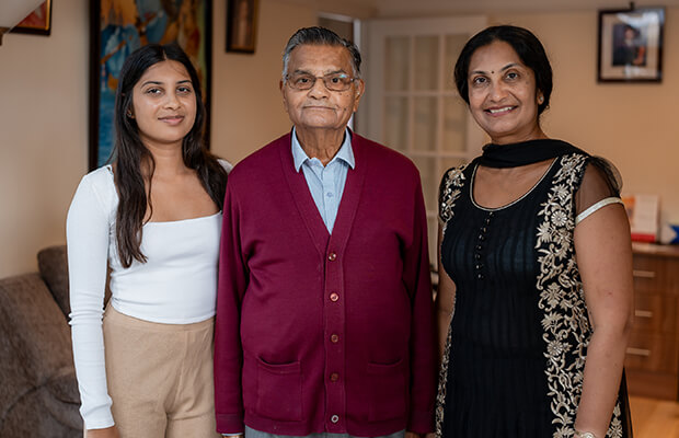 Hina Shah stands next to her father-in-law and daughter inside her living room