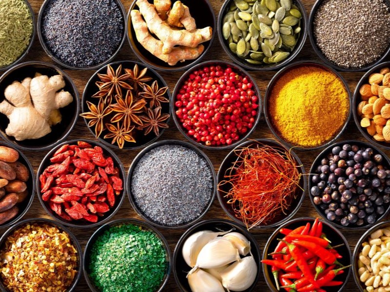 Top view of different herbs and spices in bowls on a wooden table.