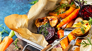 Silver baking tin containing roasted vegetables on brown baking paper