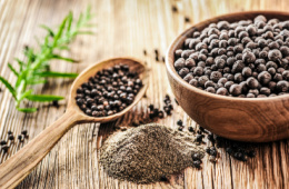 Ground black pepper next to a spoon and bowl of whole black peppercorns