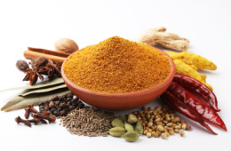 Ground garam masala in a bowl surrounded by different whole herbs and spices
