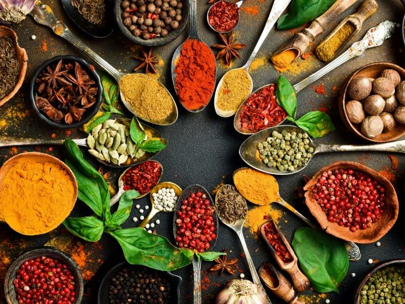 Many types of herbs and spices laid out on a wooden table.