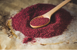 Ground sumac on a wooden spoon on a larger heap of more sumac